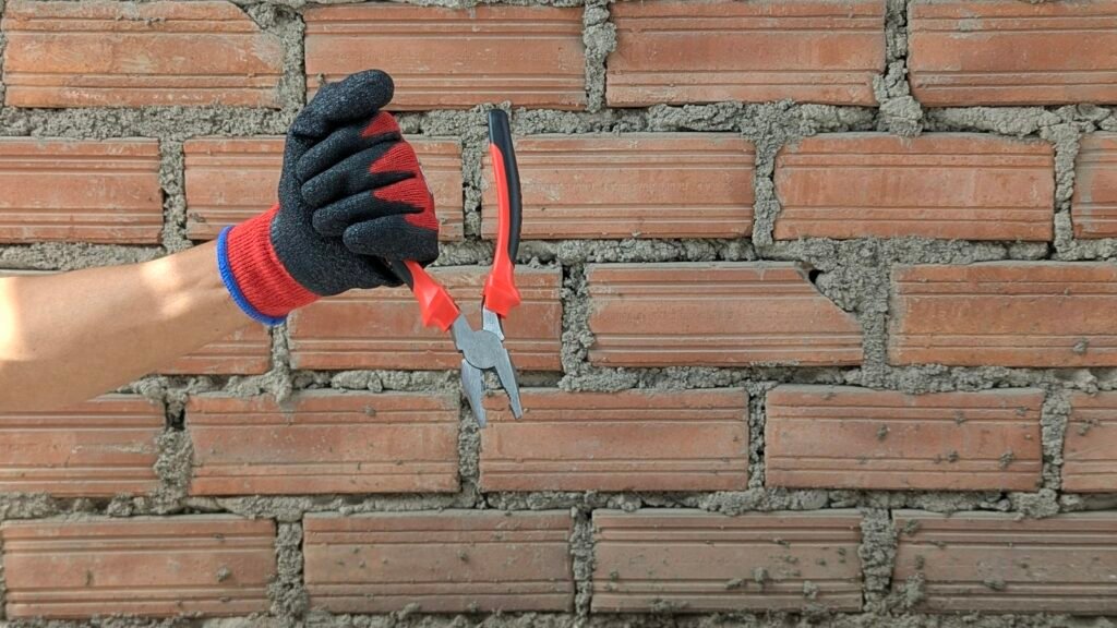 Mano con guante trabajando en una pared de ladrillo