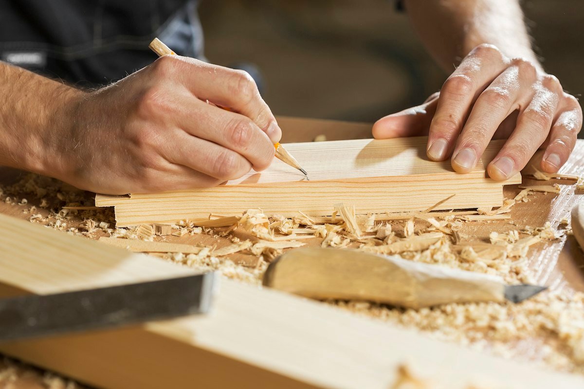Manos marcando una pieza de madera con un lápiz
