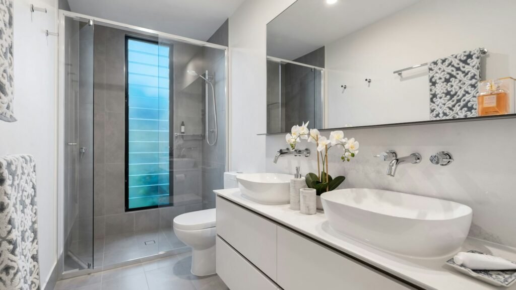Baño reformado con azulejos claros, lavabo sobre encimera y ducha