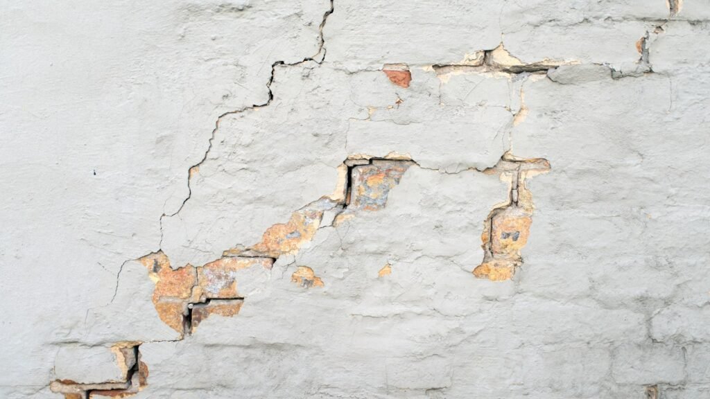 Pared de yeso agrietada con el ladrillo asomando
